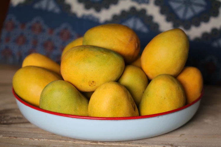 A bowl of mangos sitting on a wooden table.