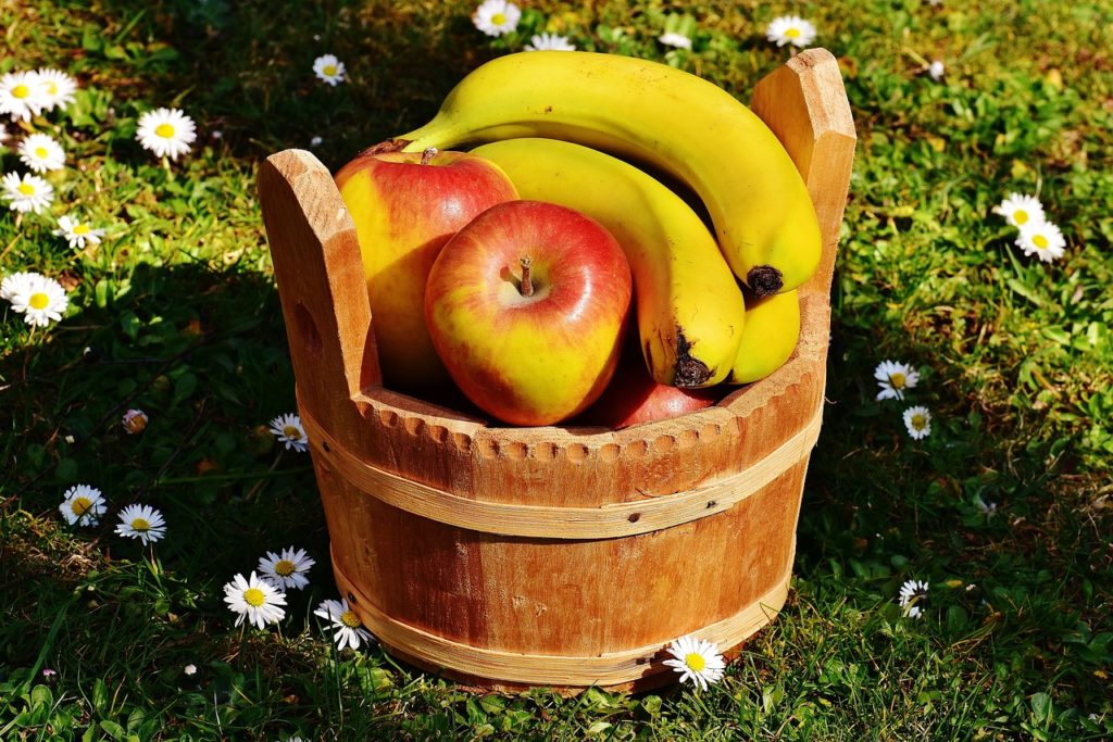 apples and bananas in a wooden bucket on the grass